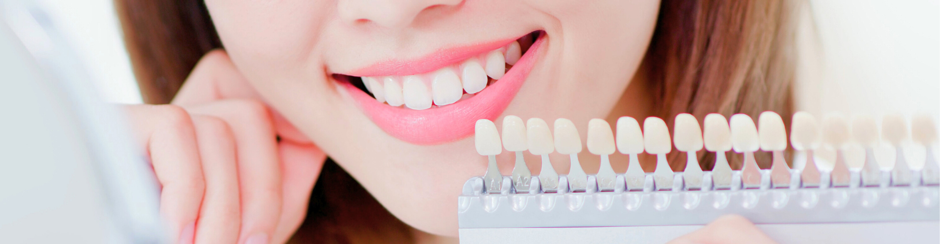 Hand holding tooth shade-matching tool next to woman's smile.
